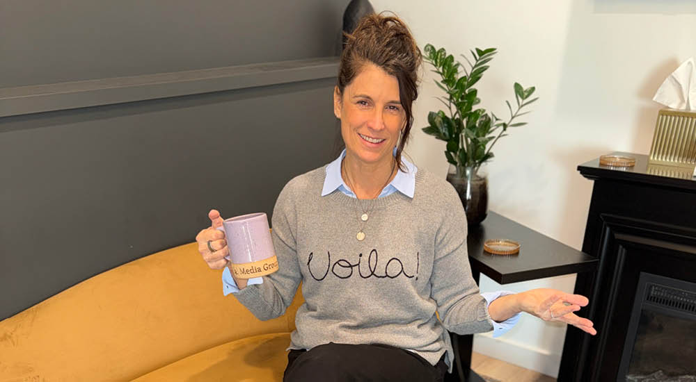 Shelly from Voila Media Group smiling on a couch with a coffee mug, ready to fix your website copy